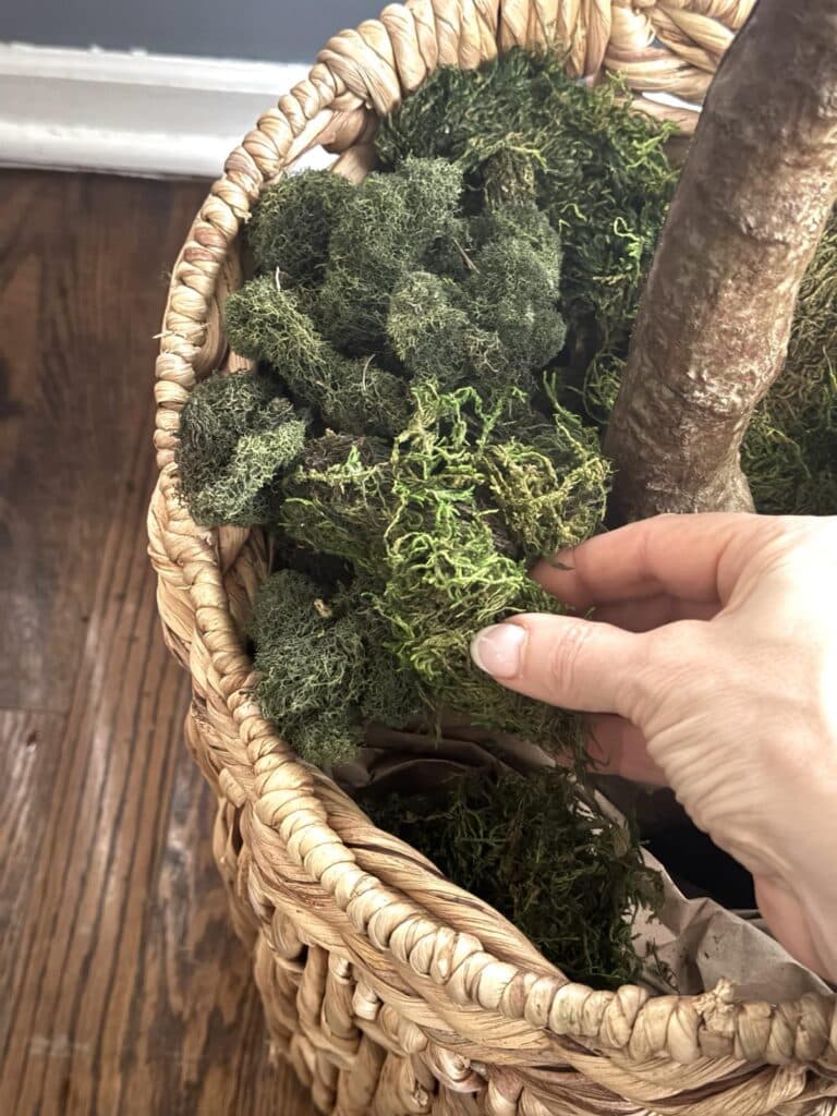 Layering green moss around the base of a decorated faux tree.