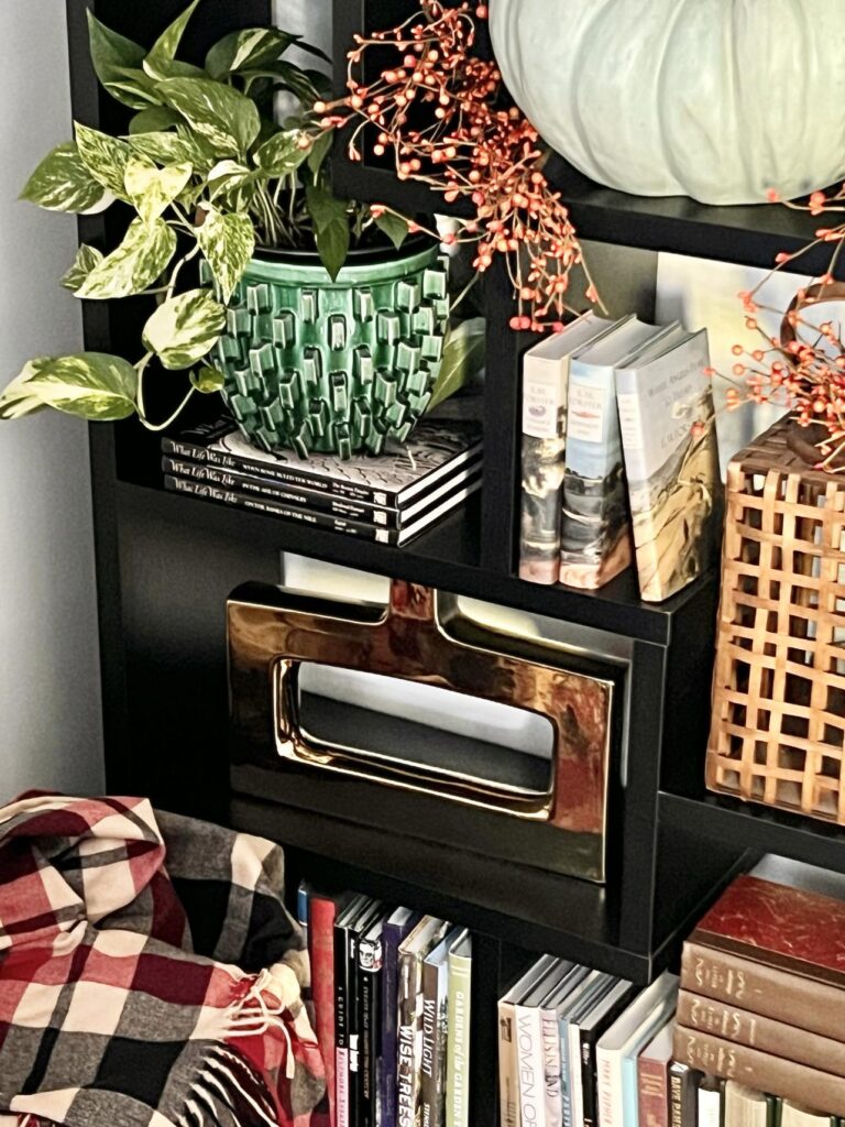 A bookshelf decorated for fall with a plaid throw blanket and wood lattice laantern.