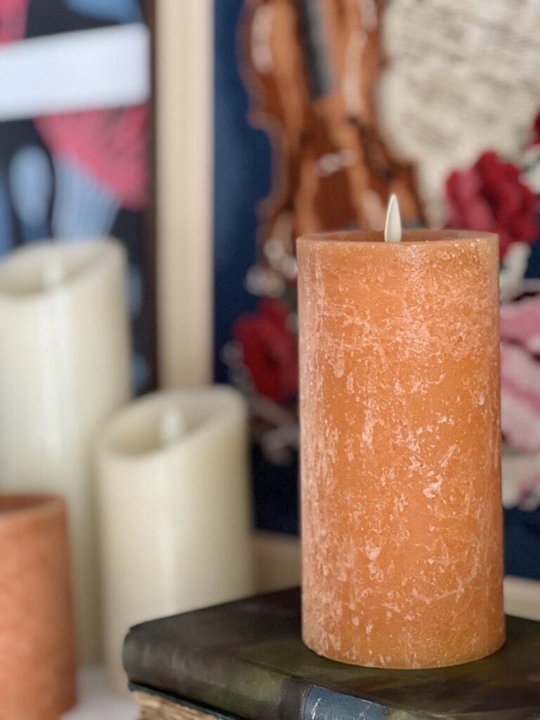 A faux pillar candle sitting on a bookshelf for ffall decorating.