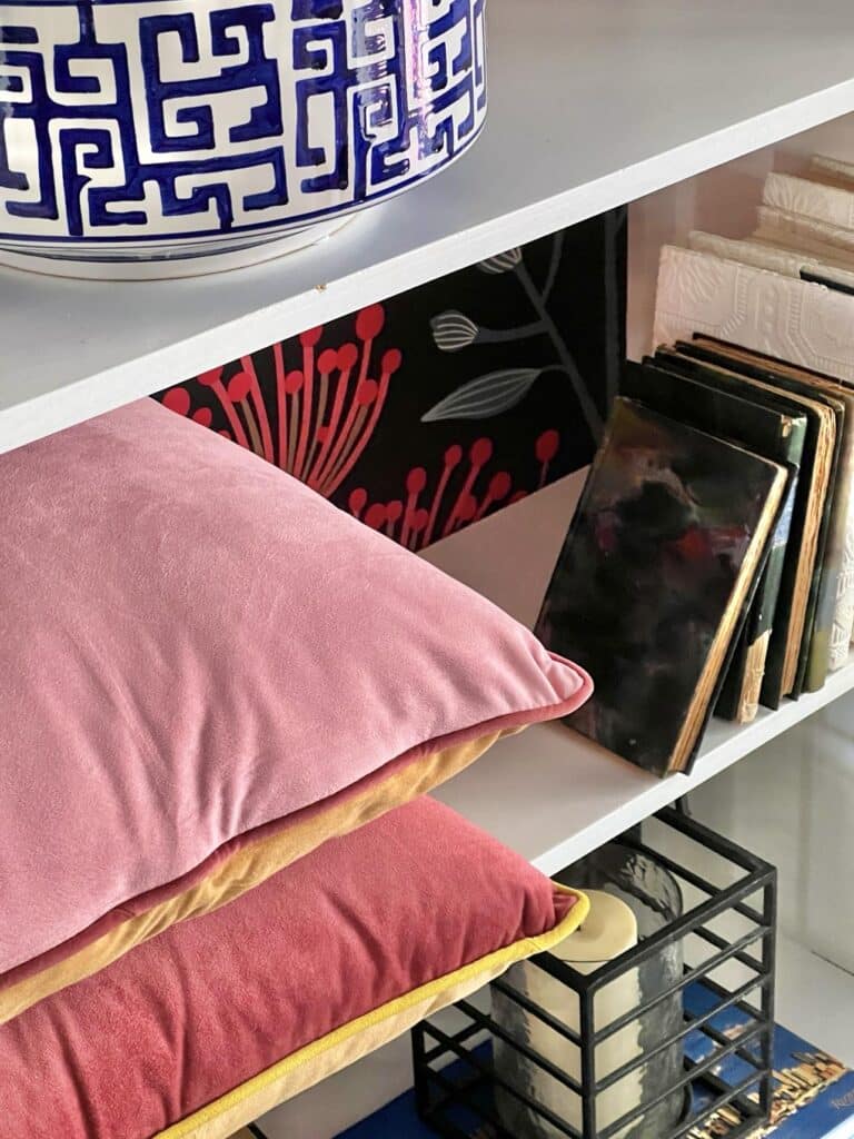 Two stacked velvet pillows sitting on a bookshelf.