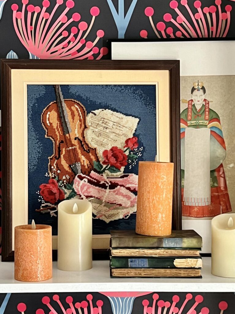 decorating bookshelves for fall with multiple faux pillar candles sitting on a shelf in front of a needlepoint wall art piece.