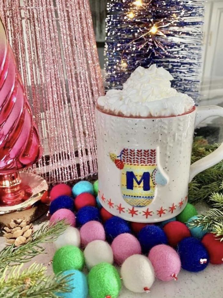 A mug of hot chocolate sitting on top of a wool felt ball trivet.