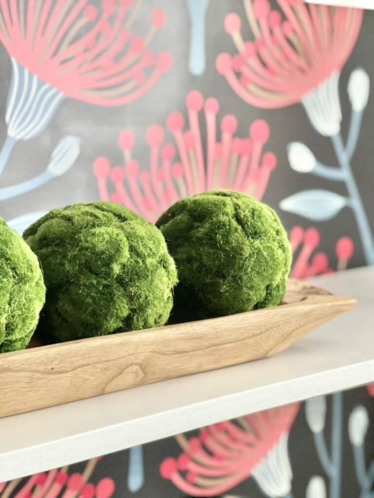 Three green moss balls decorating a dough bowl on a bookshelf.