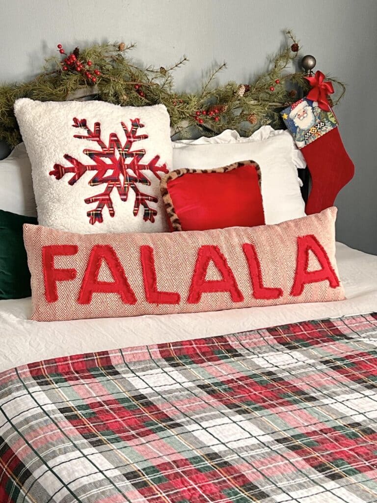 Fa La La Christmas pillow on a bed with a red plaid coverlet using a red, green and shite Christmas color scheme.