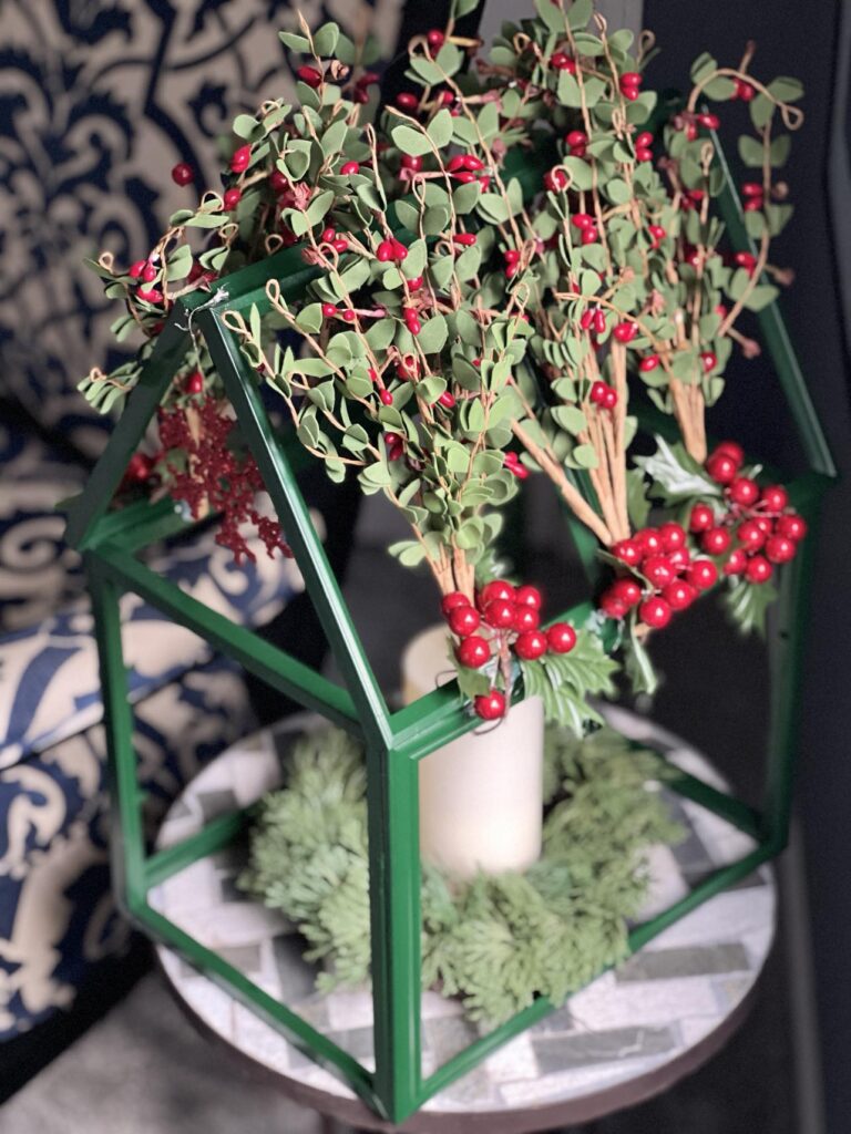 A DIY tabletop greenhouse with a greenery covered roof.