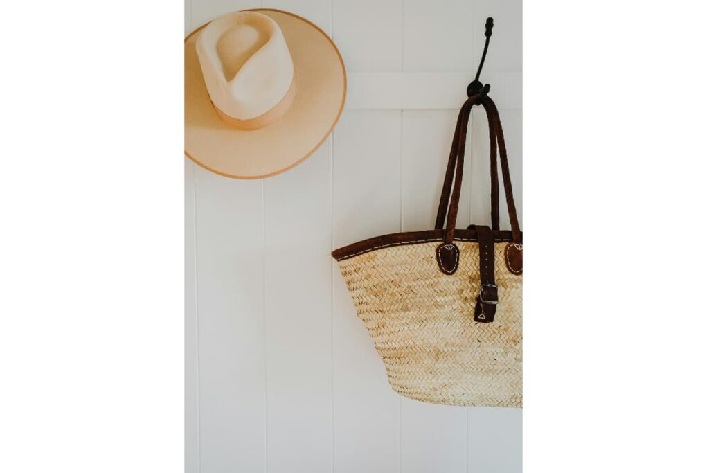 A straw hat and woven bag hanging on a hook.