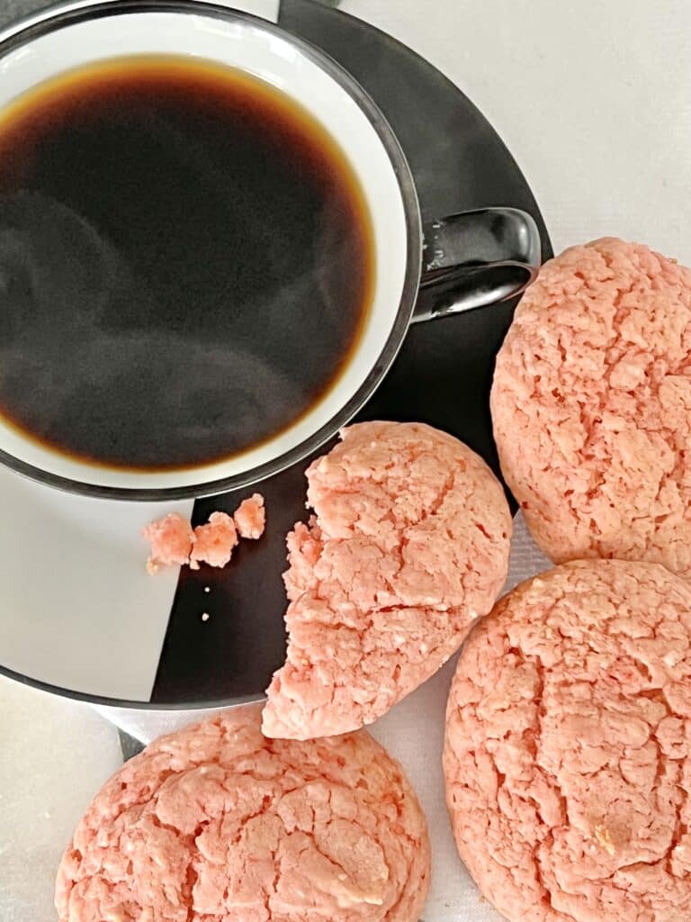 A cup of black coffee with some pink cookies.