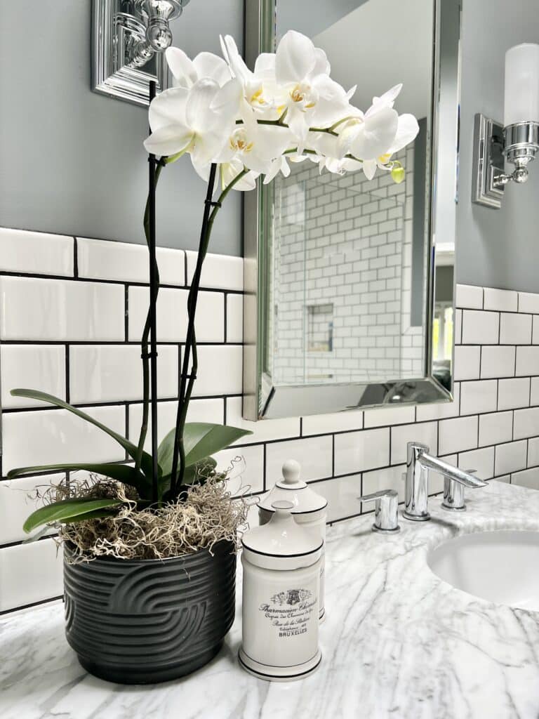 https://www.sonatahomedesign.com/wp-content/uploads/2023/07/White-orchid-in-black-candle-jar-Sonata-Home-Design-768x1024.jpg