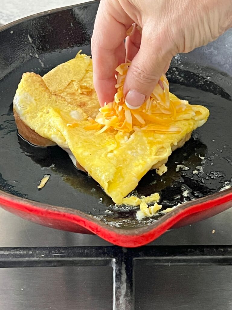 Sprinkling cheese onto eggs for one pan sandwich.