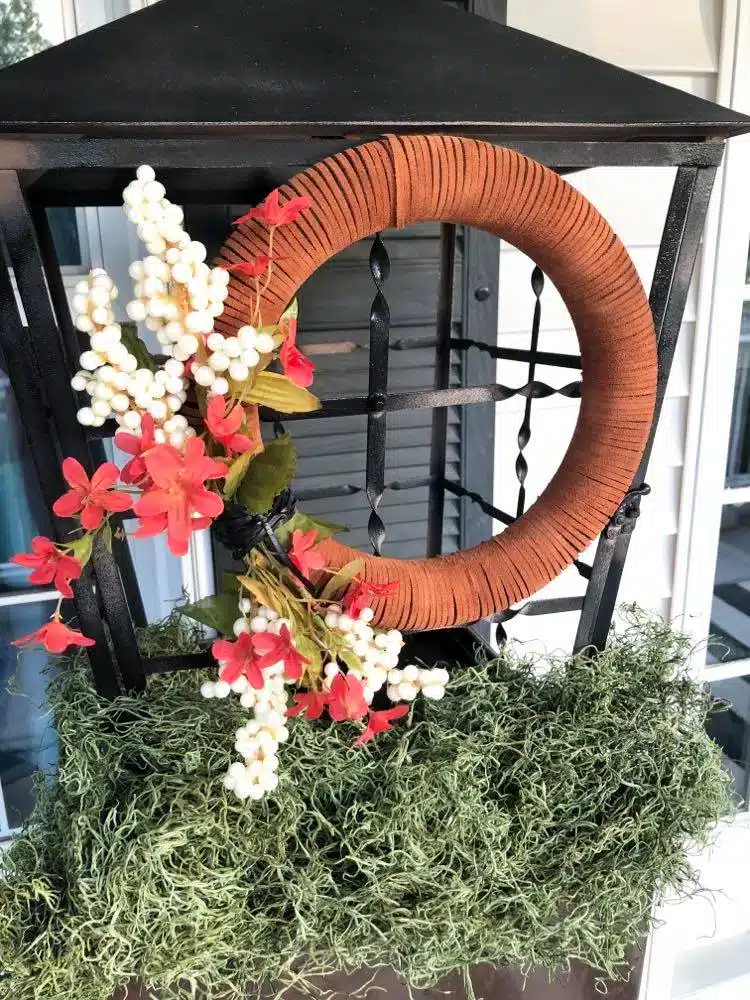 fall front porch decorating ideas on a budget include hanging a leather wreath o the front of a black lantern.