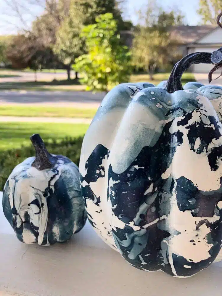 fall front porch decorating ideas on a budget include blue and white abstract painted pumpkins sitting on a porch railing.