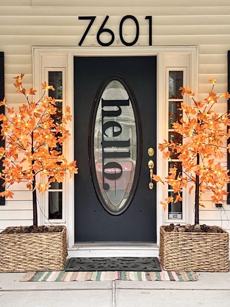 Two faux fall maple trees in baskets beside a front porch door.