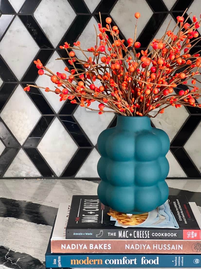 https://www.sonatahomedesign.com/wp-content/uploads/2023/09/Orange-pip-berries-in-a-blue-vase-on-top-of-stacked-cookbooks-Sonata-Home-Design.jpg