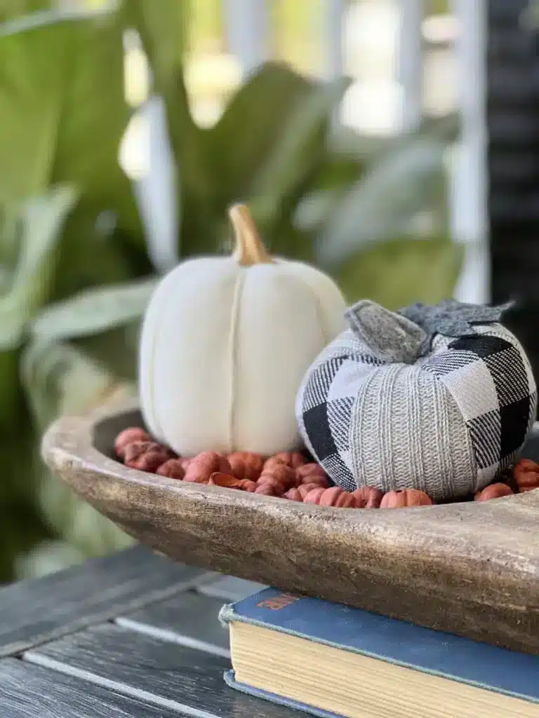 fall front porch decorating ideas on a budget includes layering faux white, orange and plaid pumpkins in a dough bowl and displaying on a porch side table.