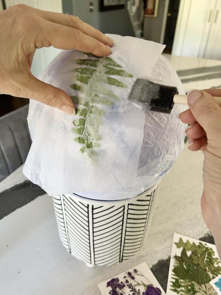 Brushing glue over tissue covered pressed leaf to create a DIY paper lantern.