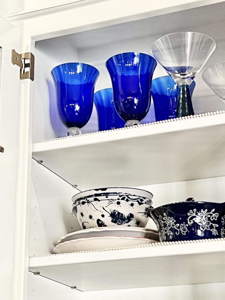 Cobalt blue glasses displayed on the top shelf of a kitchen cabinet with a glass door.