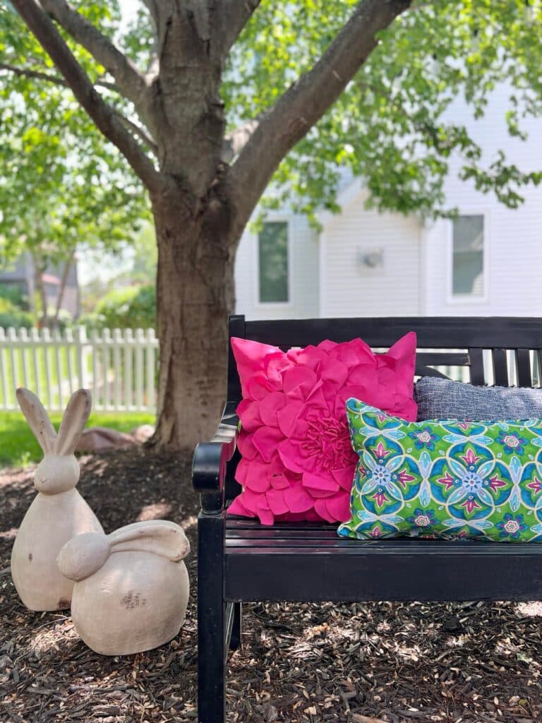 Colorful pink and blue pillows on a black bench in a shade garden.