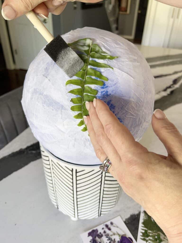 Gluing a fern leaf to a tissue paper covered lantern shape.