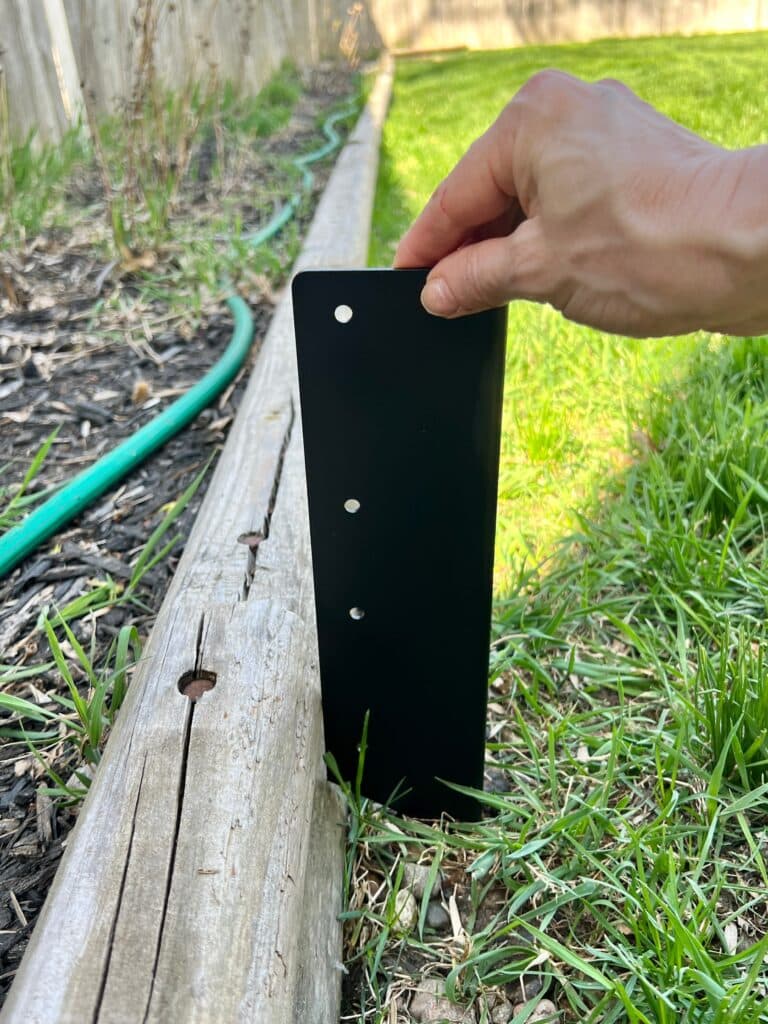 Holding a Toja Grid bracket upright to measure the height of the easy raised garden bed.
