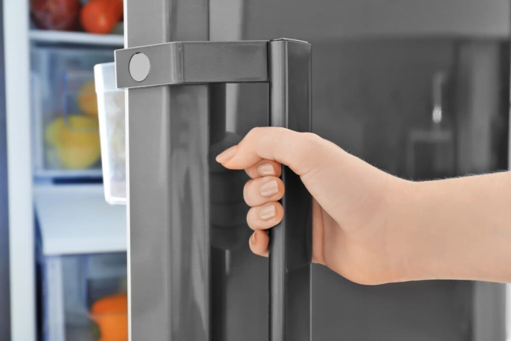 A woman's hand opening a refrigerator door.