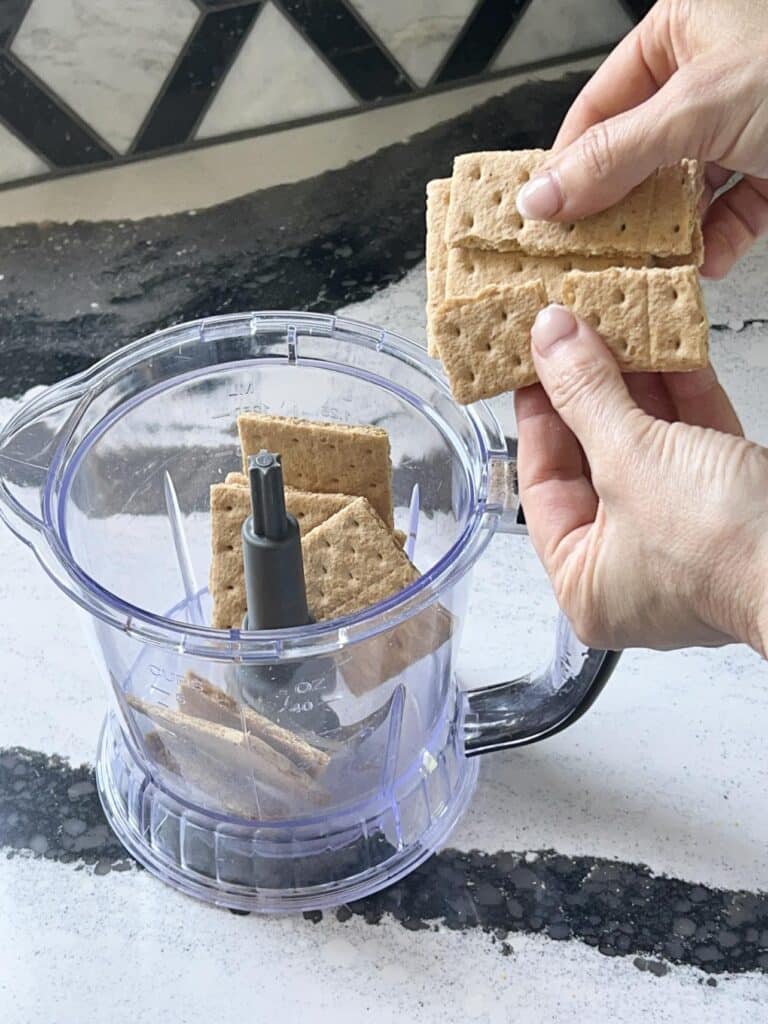 Breaking graham crackers into a food processor.