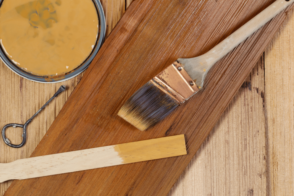 A paintbrush, wood stain, and cedar lumber.