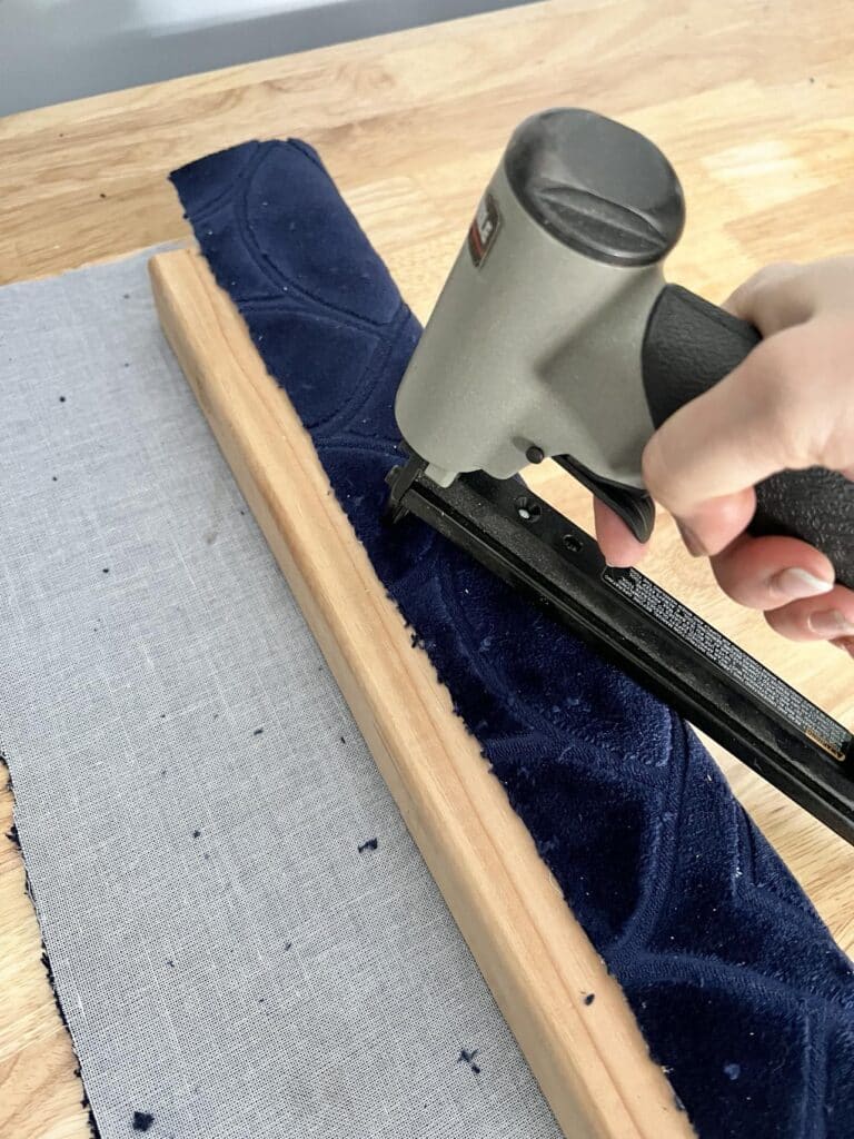 Stapling fabric to a 2 x 4 piece of wood.