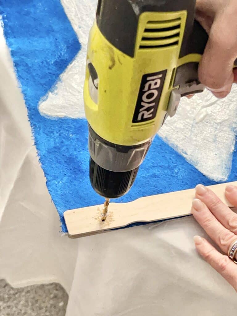 Drilling a hole toward the end of the glued paint stir sticks.