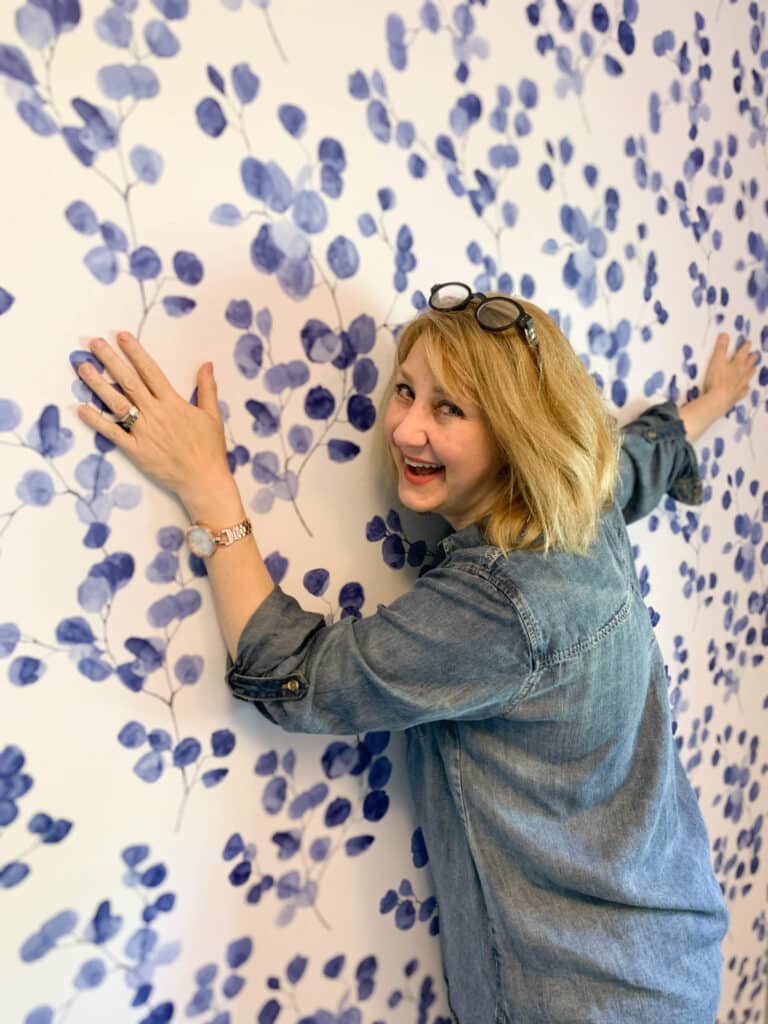 Woman hugging a wall that has been covered with blue and white peel and stick wallpaper.