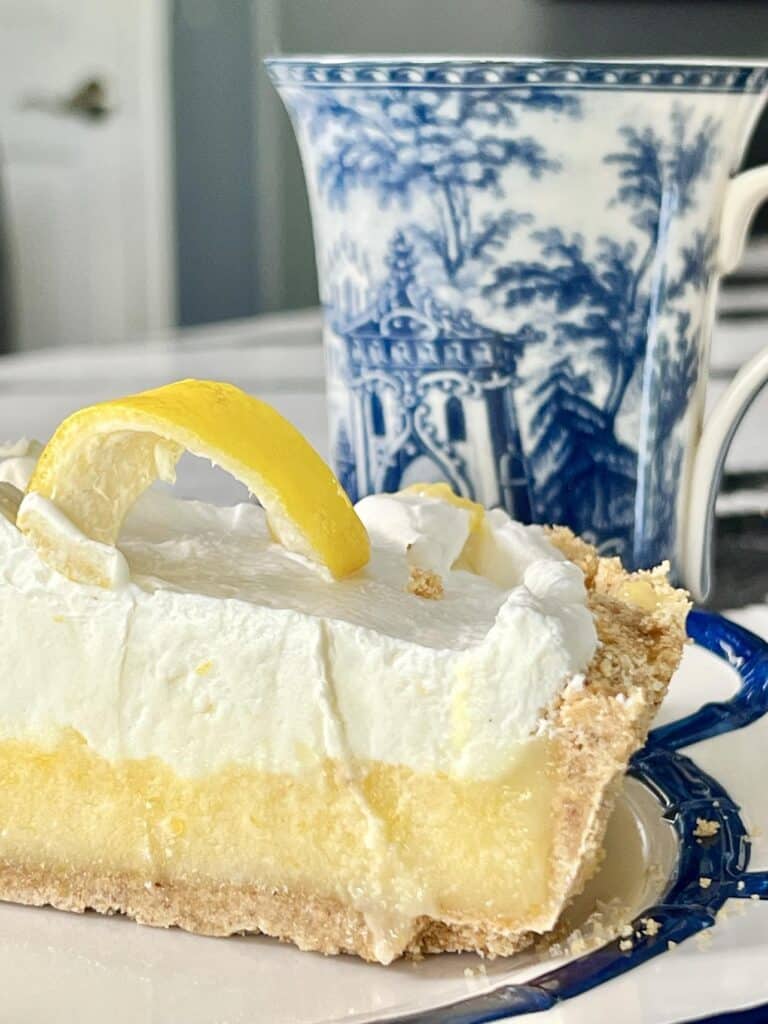 A slice of lemon curd pie no bake on a plate with a cup of coffee.