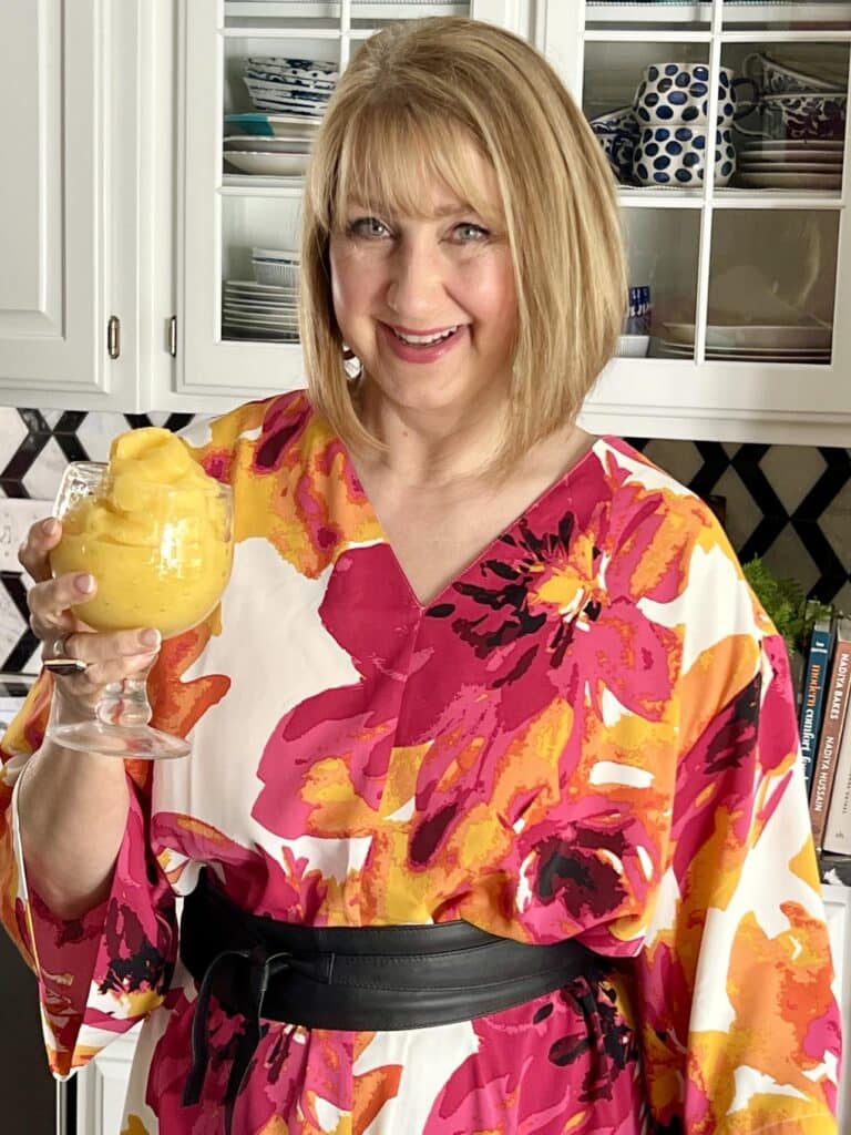 A woman in aa red and orange dress holding a glass goblet full of the mango a go go smoothie drink.