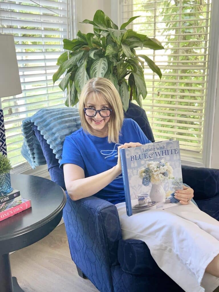 A woman sitting in a blue chair reading a coffee table book about decorating with blue and white.