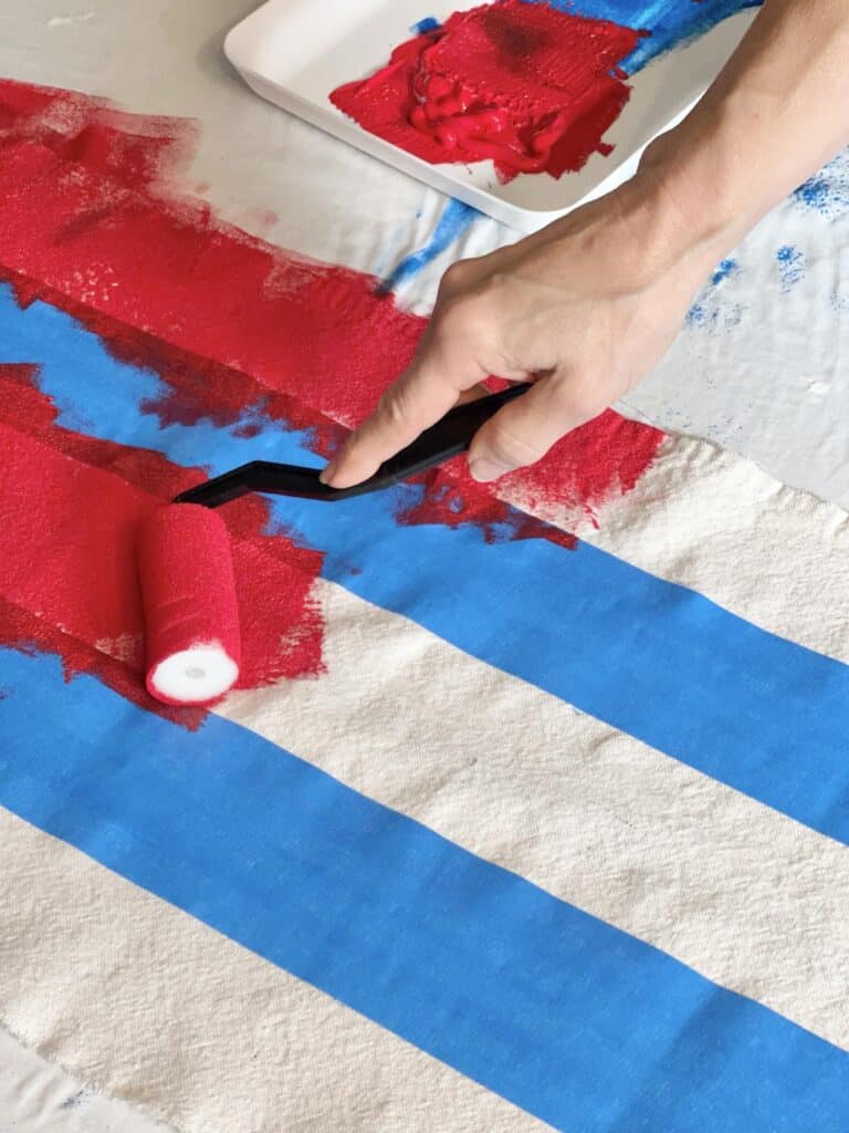Painting red stripes onto the DIY Flag Banner with a paint roller.