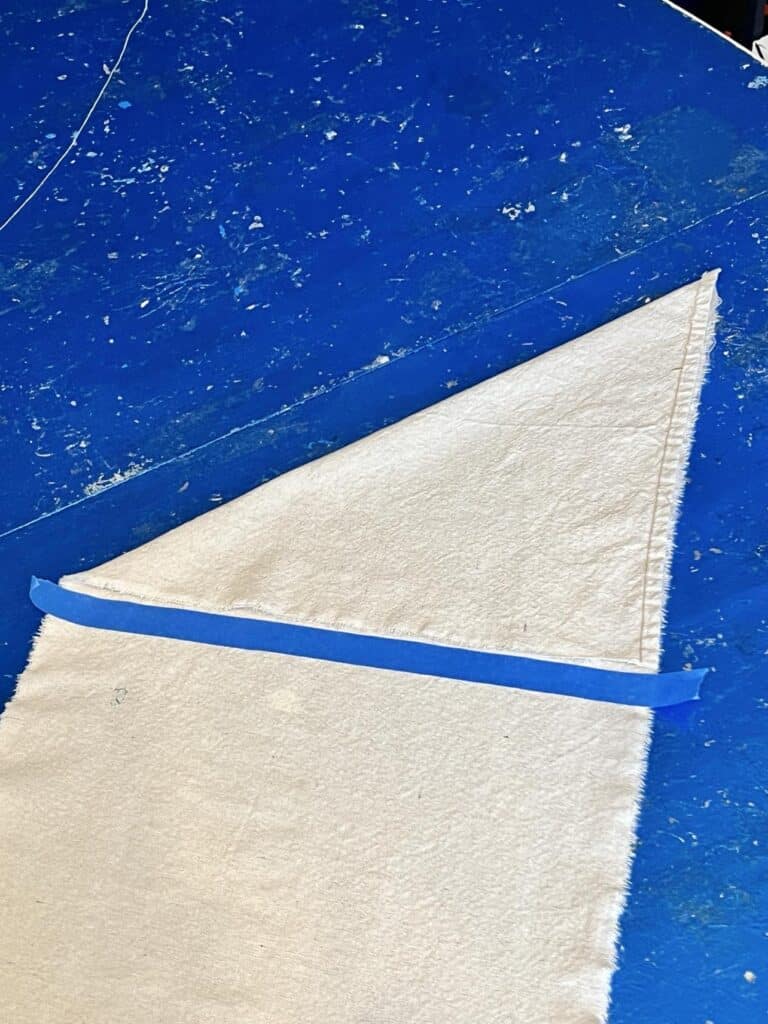 Placing a piece of painters tape across the bottom of the fabric triangle for make the top of the banner.