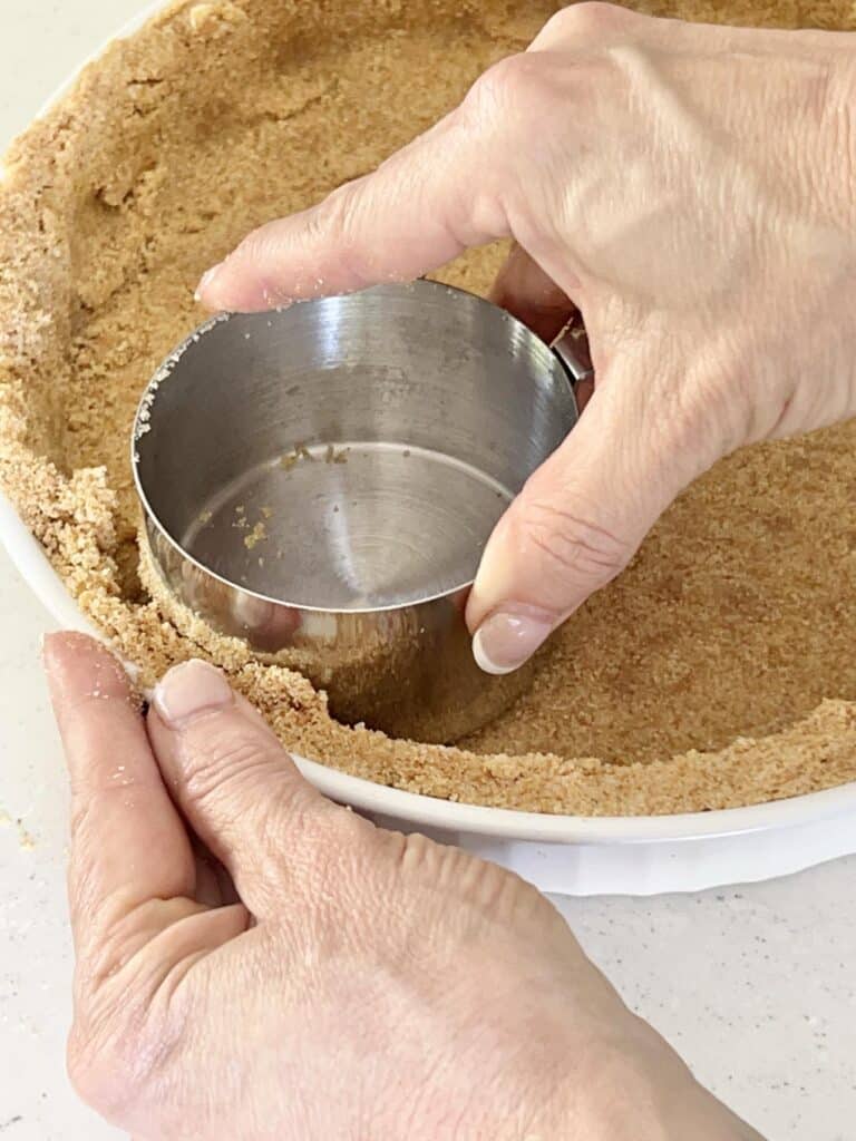 Pressing the graham crumbs into a tart pan with the bottom of a measuring cup.