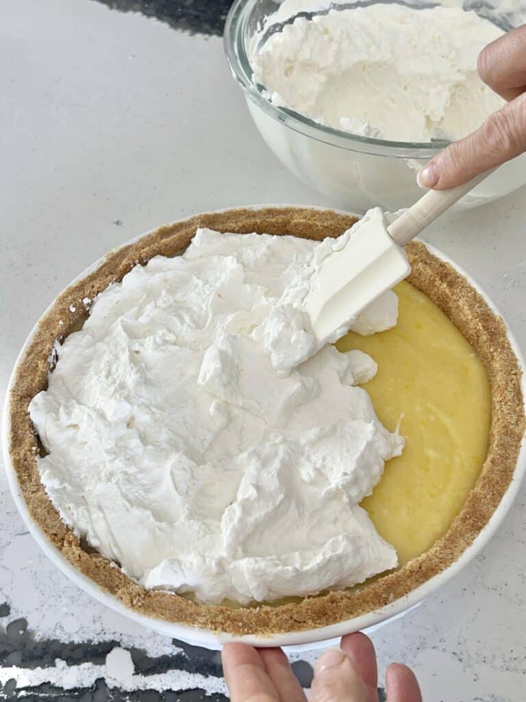 Spreading whipped topping to the top of the no bake lemon curd pie.