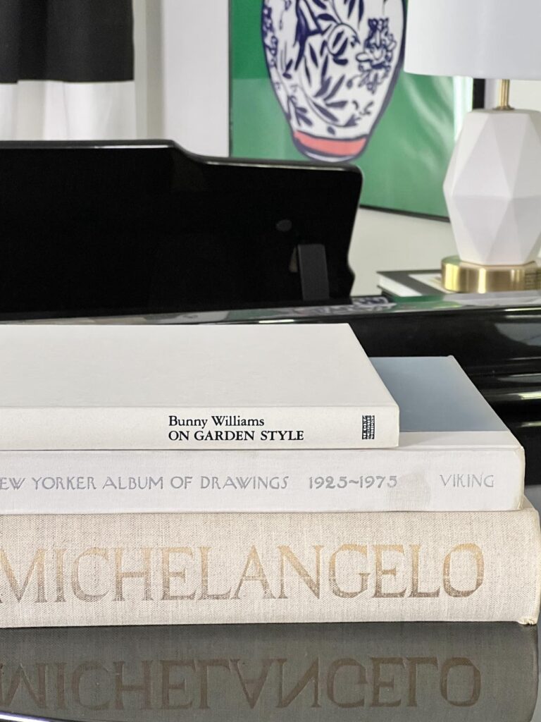 A stack of three cream colored art books decorating the top of a piano.