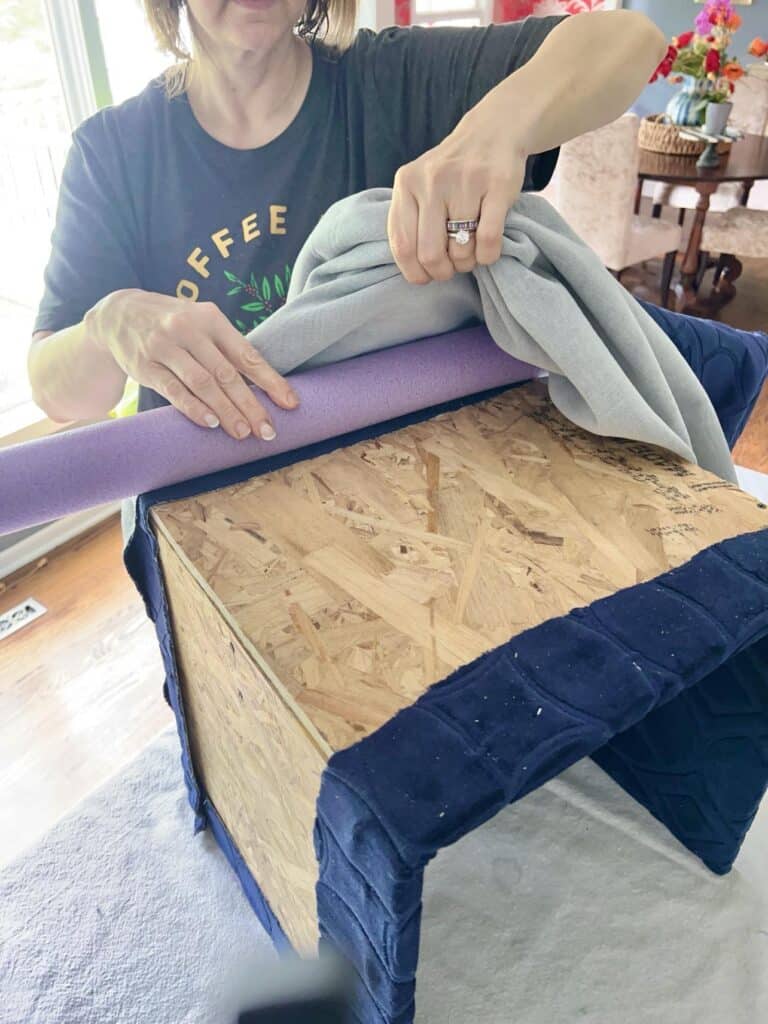 Tucking a pool noodle inside fabric for a diy coffee table ottoman.