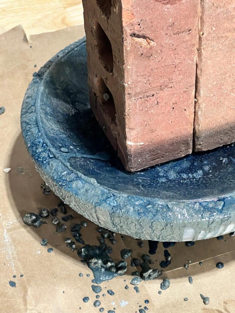 Two bricks holding a glass plate in place on top of aa DIY concrete bowl.