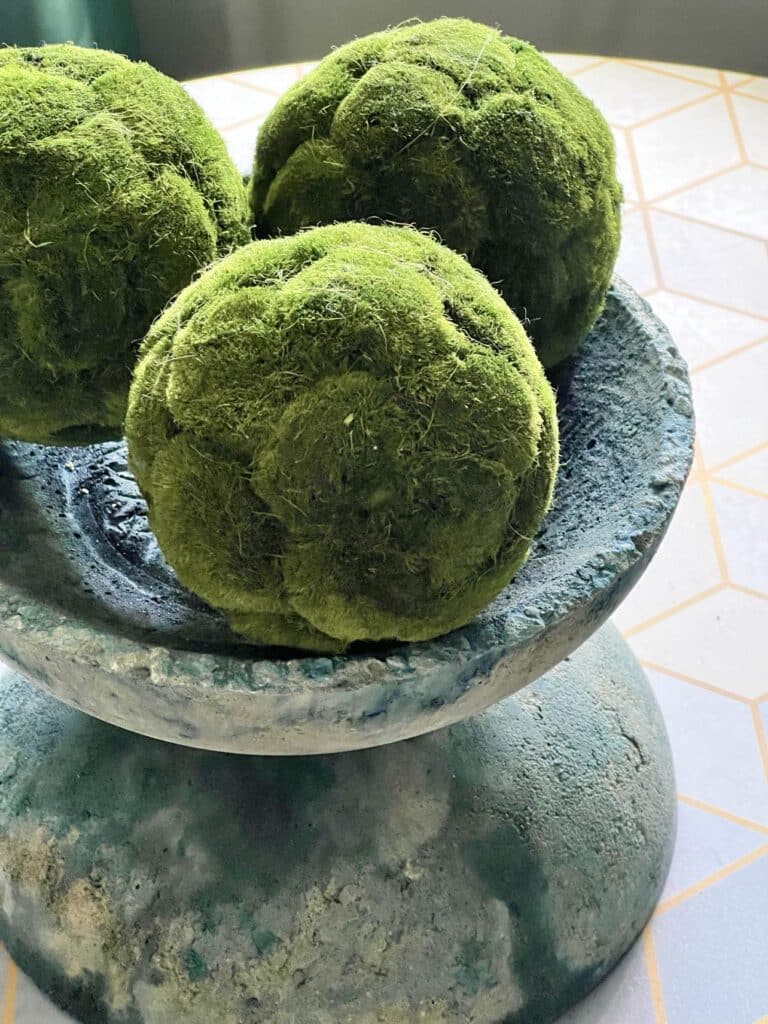 Three green moss balls sitting inside the DIY concrete bowl.