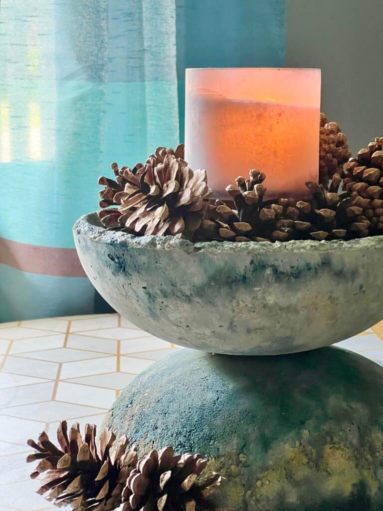 A DIY concrete bowl styled with a pillar candle and pine cones.