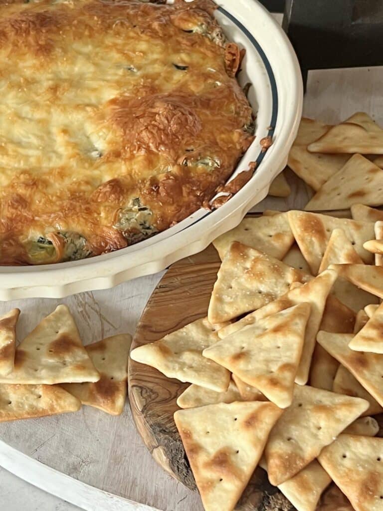 Baked spinach artichoke dip in a pie plate served with pita chips.