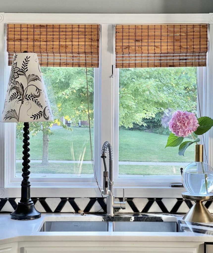 A kitchen sink flanked by a lamp and a single hydrangea bloom.