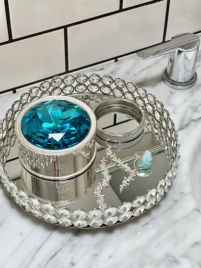 A glass tray holds a small jewelry box, a bracelet, earrings, and a blue ring.