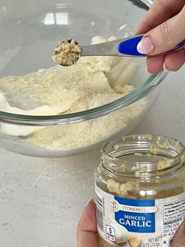 Measuring mince garlic into a bowl.