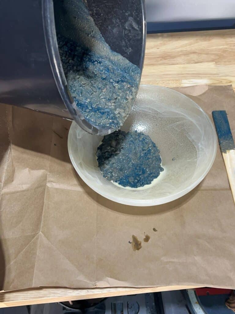 Pouring blue tinted concrete mix into a prepared glass bowl.