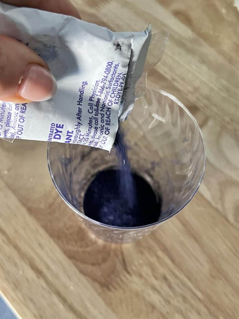 Pouring blue fabric dye powder into a plastic cup.