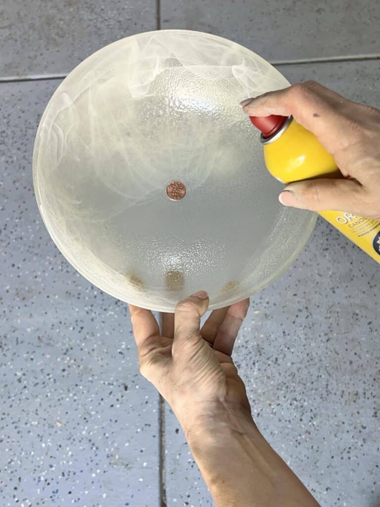 Spraying a glass fixture cover with cooking spray for a DIY concrete bowl.