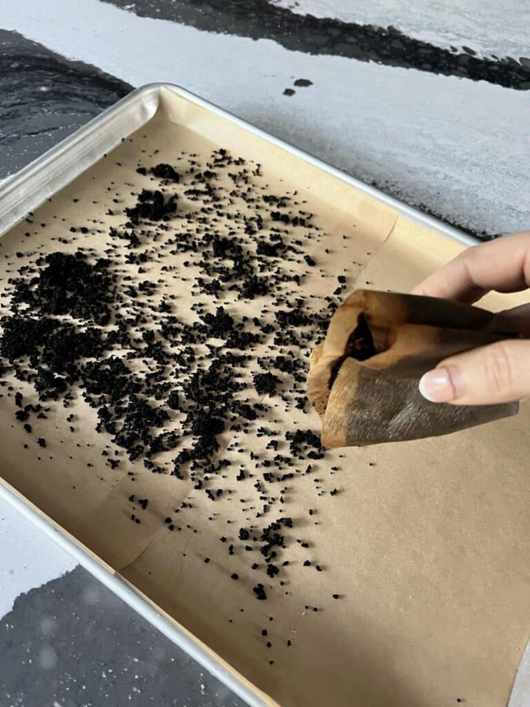 Sprinkling coffee grounds on parchment paper to dry.