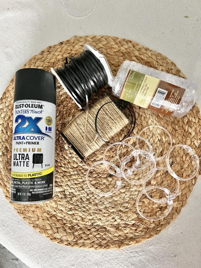 Supplies for a DIY lazy Susan that includes a woven placemat, black spray paint, plastic curtain rings, and jute twine.